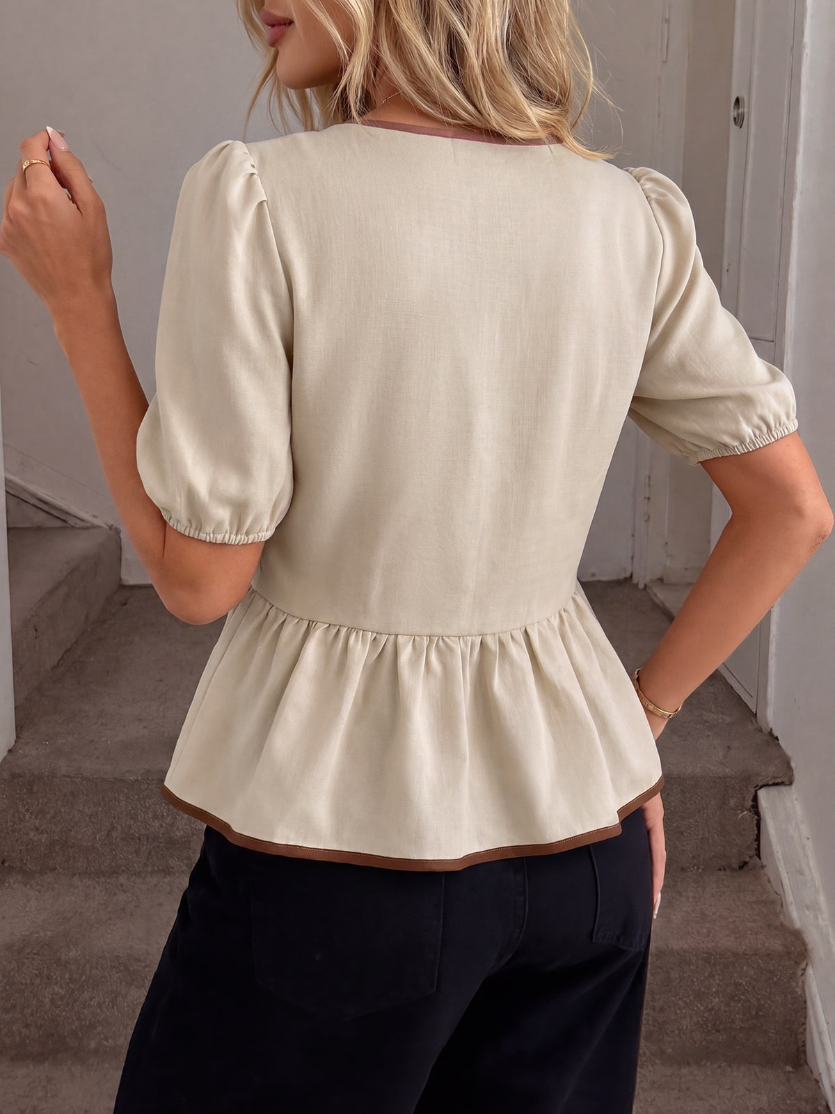 Back view of beige puff sleeve peplum top with brown piped hem